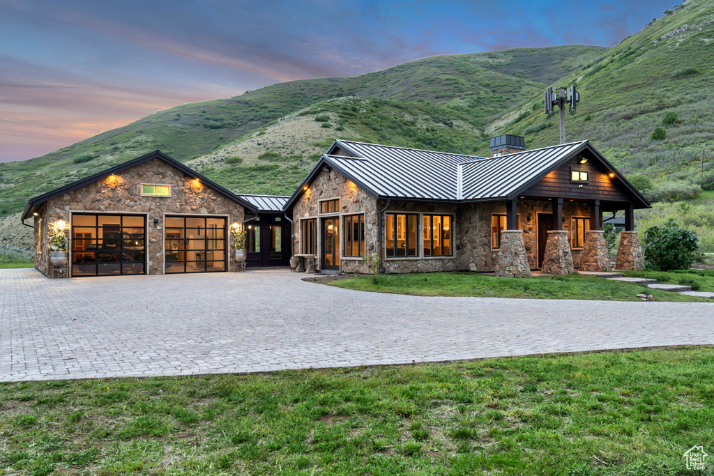 View of front of home with a standing seam roof, stone siding, an attached garage, and decorative driveway