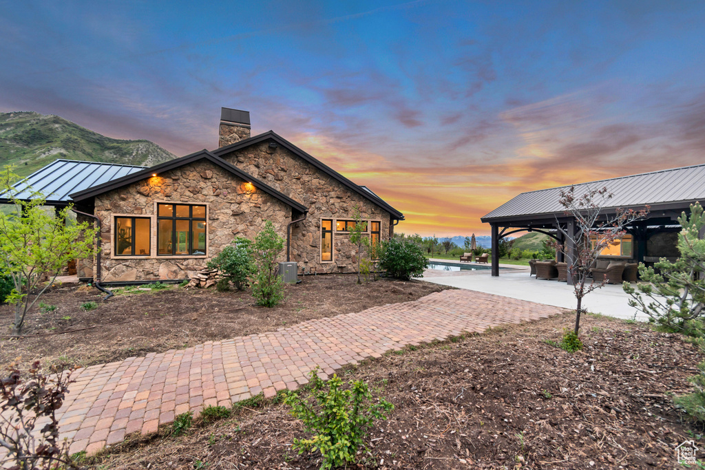 View of side of property featuring a chimney, stone siding, a standing seam roof, a gazebo, and metal roof