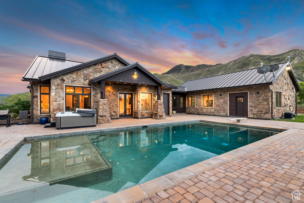 Rear view of house featuring a standing seam roof, a hot tub, a patio area, and stone siding