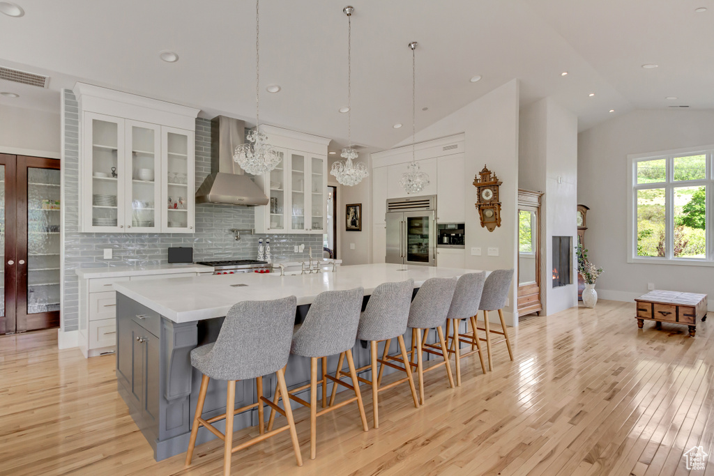 Kitchen with wall chimney exhaust hood, built in refrigerator, light countertops, light wood-style flooring, and recessed lighting