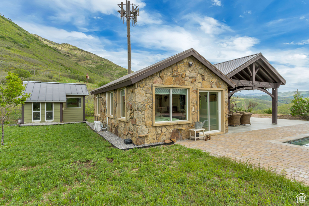 Rear view of property featuring stone siding, a patio area, a mountain view, and a lawn