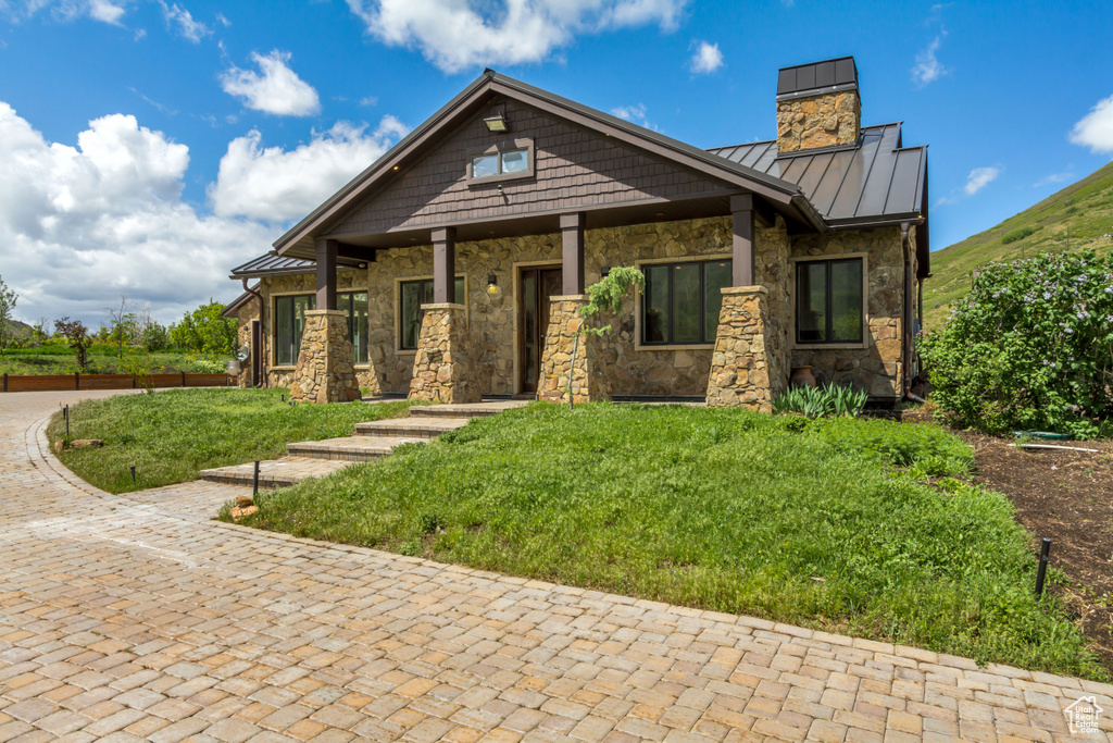 Craftsman-style house with a standing seam roof, stone siding, a chimney, metal roof, and a front yard
