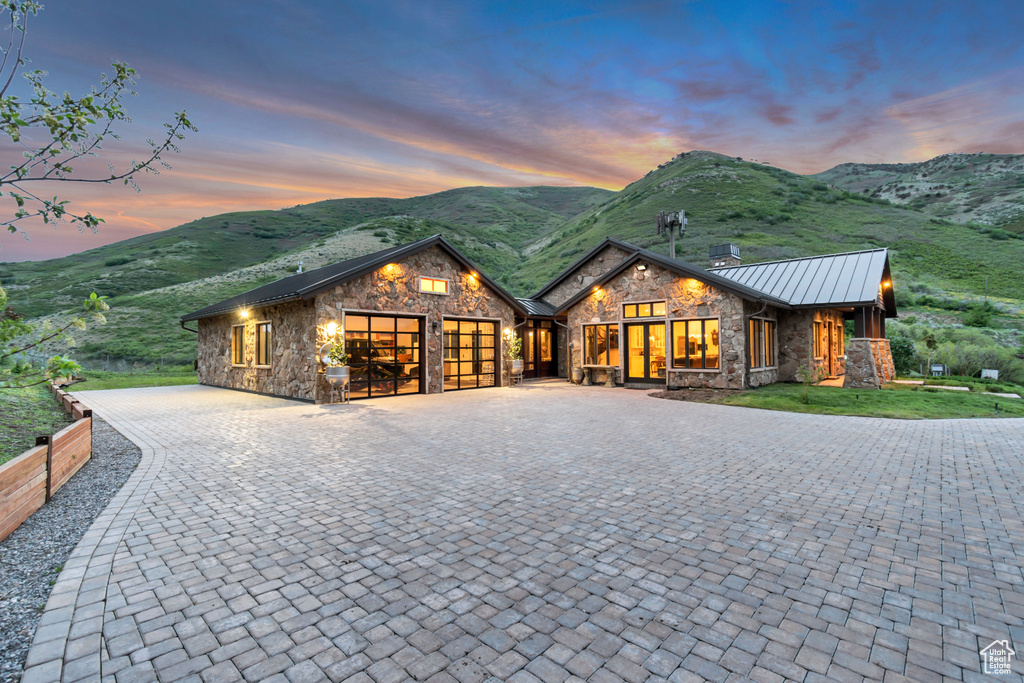 View of front of home with stone siding, curved driveway, an attached garage, a standing seam roof, and a mountain view