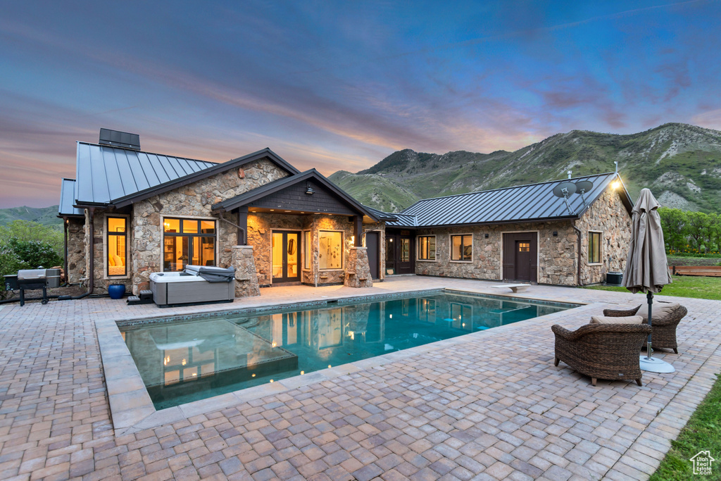 Pool at dusk with a patio area, an outdoor pool, a mountain view, and a hot tub