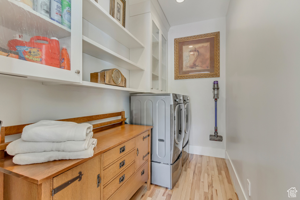 Laundry area featuring separate washer and dryer, light wood finished floors, baseboards, and cabinet space
