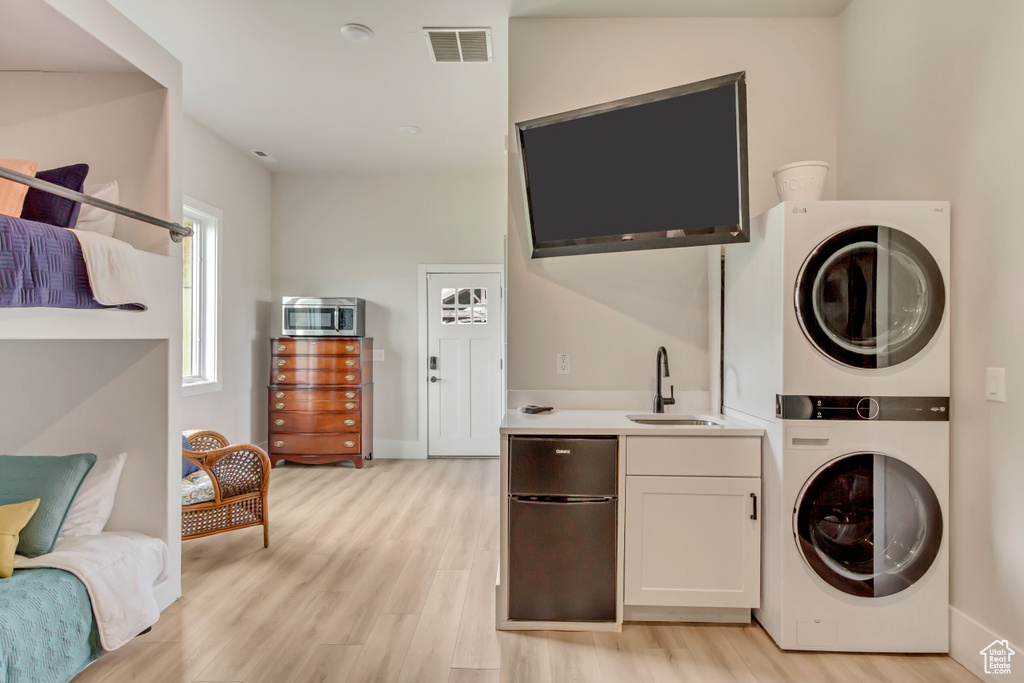 Clothes washing area featuring stacked washer and clothes dryer, light wood finished floors, baseboards, and bar with sink