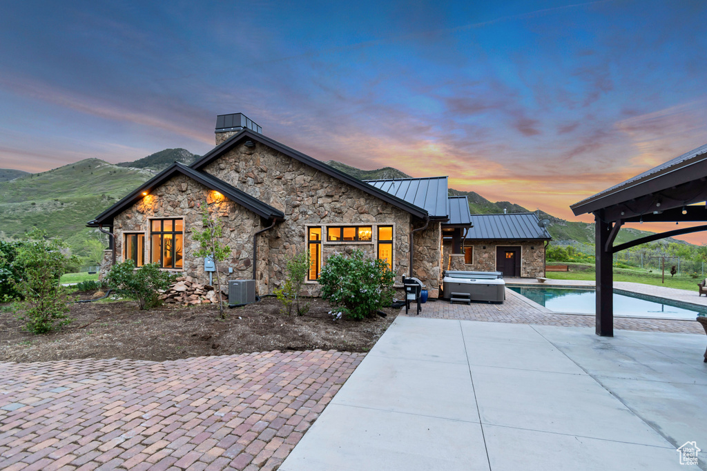 View of front of property with an outdoor hot tub, a standing seam roof, stone siding, and a patio area