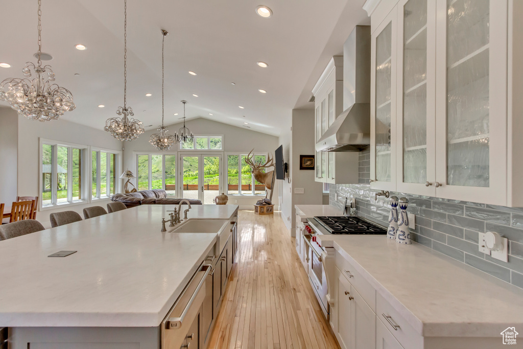 Kitchen featuring wall chimney exhaust hood, a chandelier, vaulted ceiling, a spacious island, and light wood-style floors