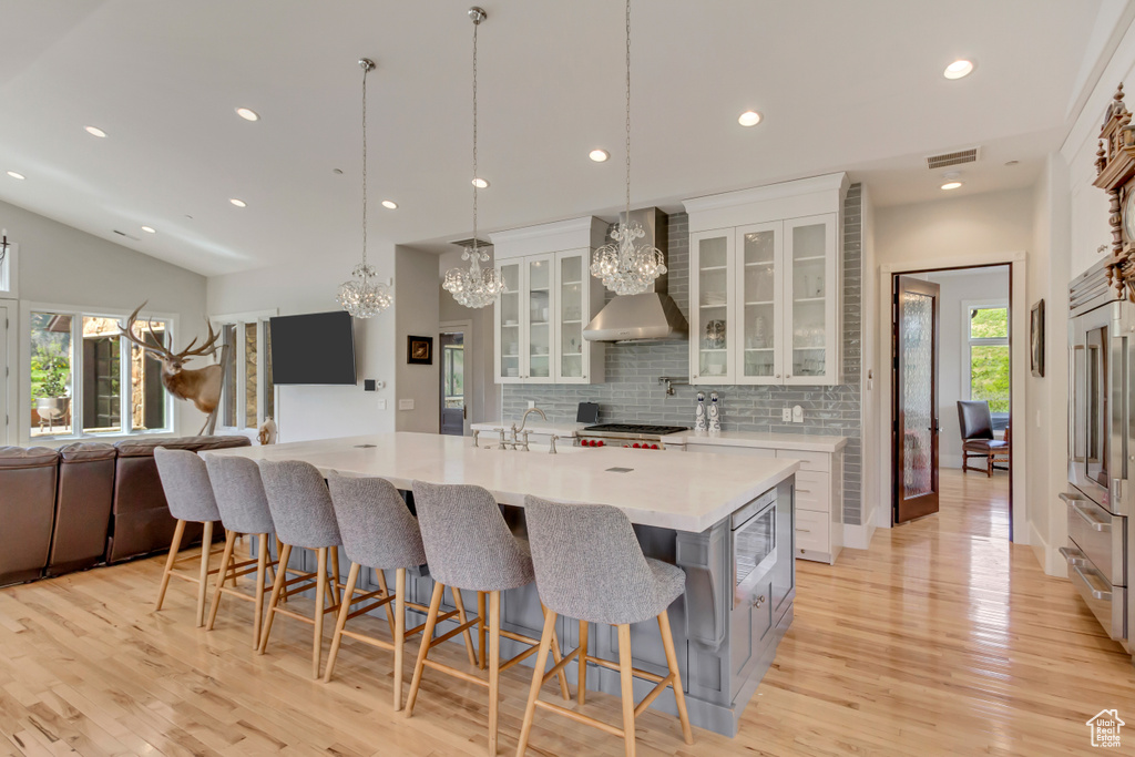 Kitchen featuring wall chimney range hood, backsplash, light wood-type flooring, recessed lighting, and white cabinetry