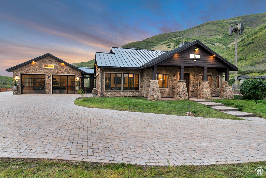 View of front facade featuring stone siding, a standing seam roof, decorative driveway, a garage, and a lawn