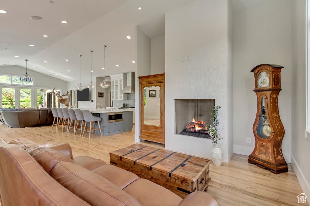 Living room featuring light wood-type flooring, high vaulted ceiling, a lit fireplace, recessed lighting, and baseboards