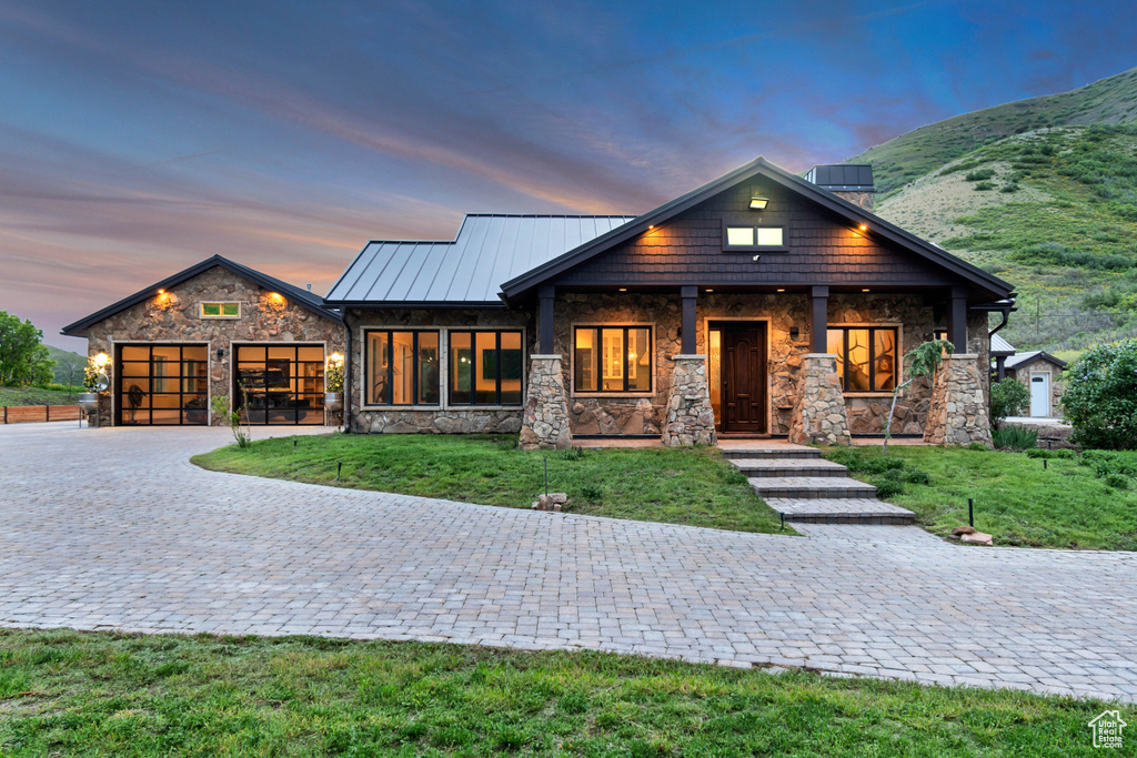 View of front facade with stone siding, decorative driveway, an attached garage, a yard, and a standing seam roof
