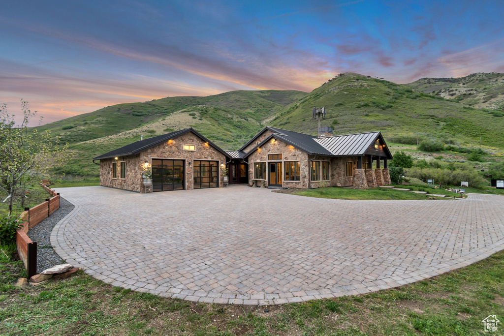 View of front of property with stone siding, a standing seam roof, a garage, a mountain view, and curved driveway