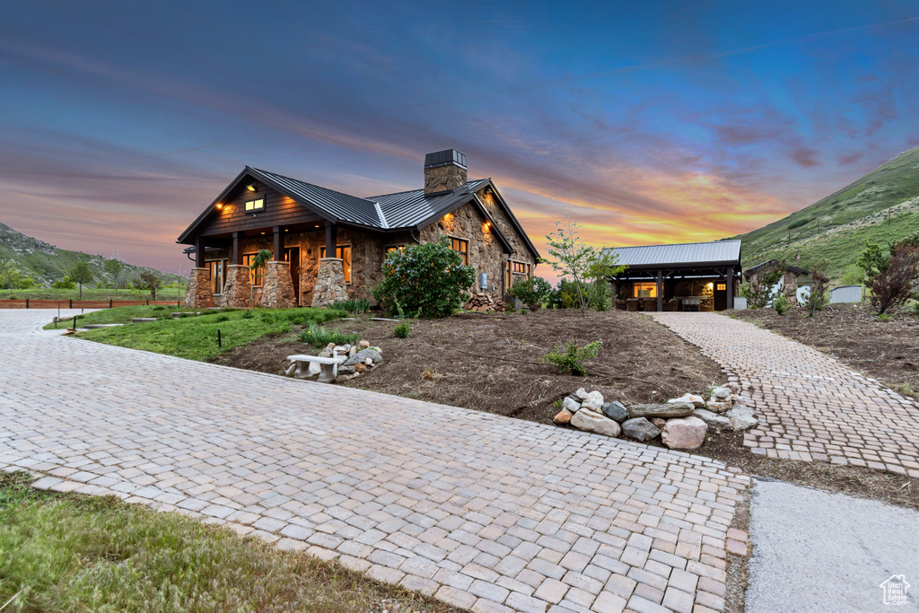 View of front of house with stone siding, a chimney, a standing seam roof, covered porch, and metal roof
