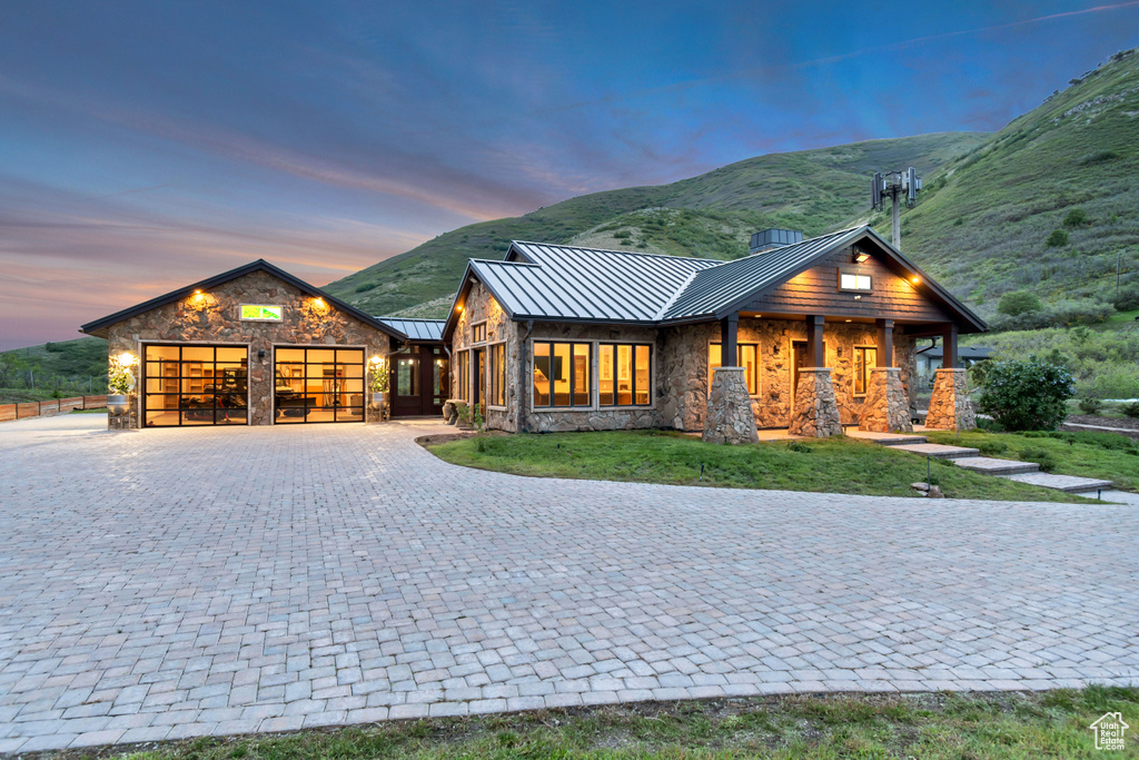 View of front of house featuring a standing seam roof, stone siding, a garage, and decorative driveway