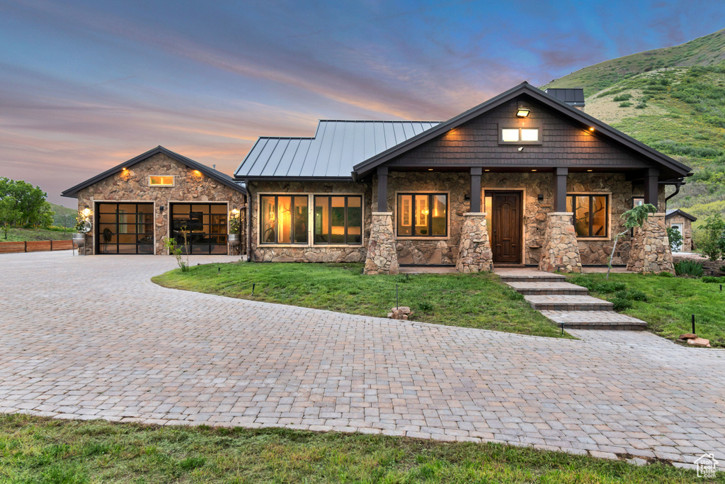 View of front of property with stone siding, decorative driveway, a lawn, a standing seam roof, and an attached garage