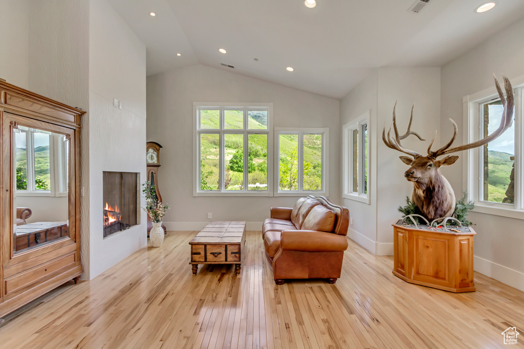 Living area with light wood finished floors, high vaulted ceiling, a lit fireplace, recessed lighting, and baseboards