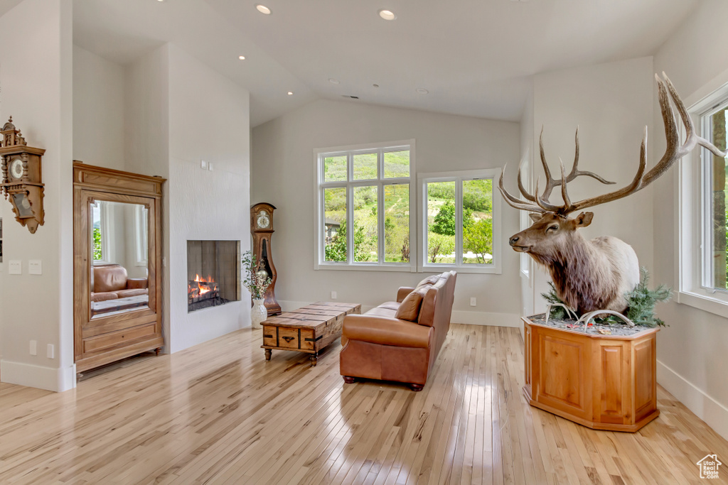 Sitting room featuring light wood-style flooring, a lit fireplace, high vaulted ceiling, baseboards, and recessed lighting