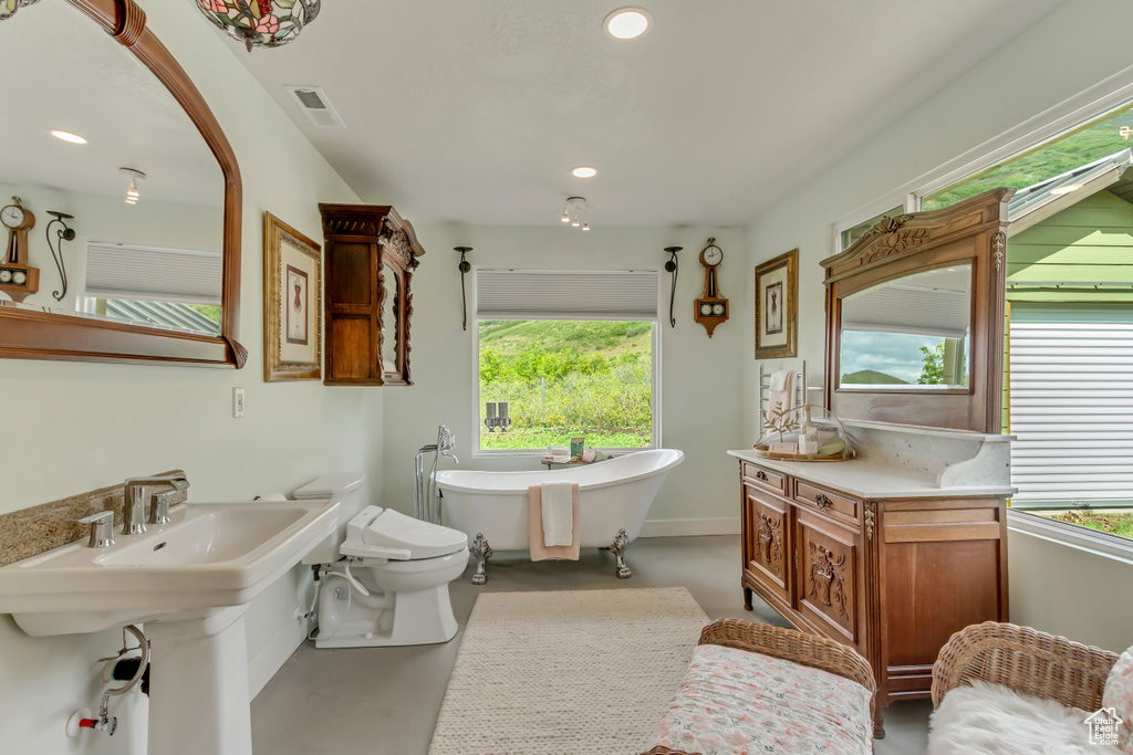 Bathroom featuring finished concrete flooring, a freestanding bath, plenty of natural light, recessed lighting, and toilet