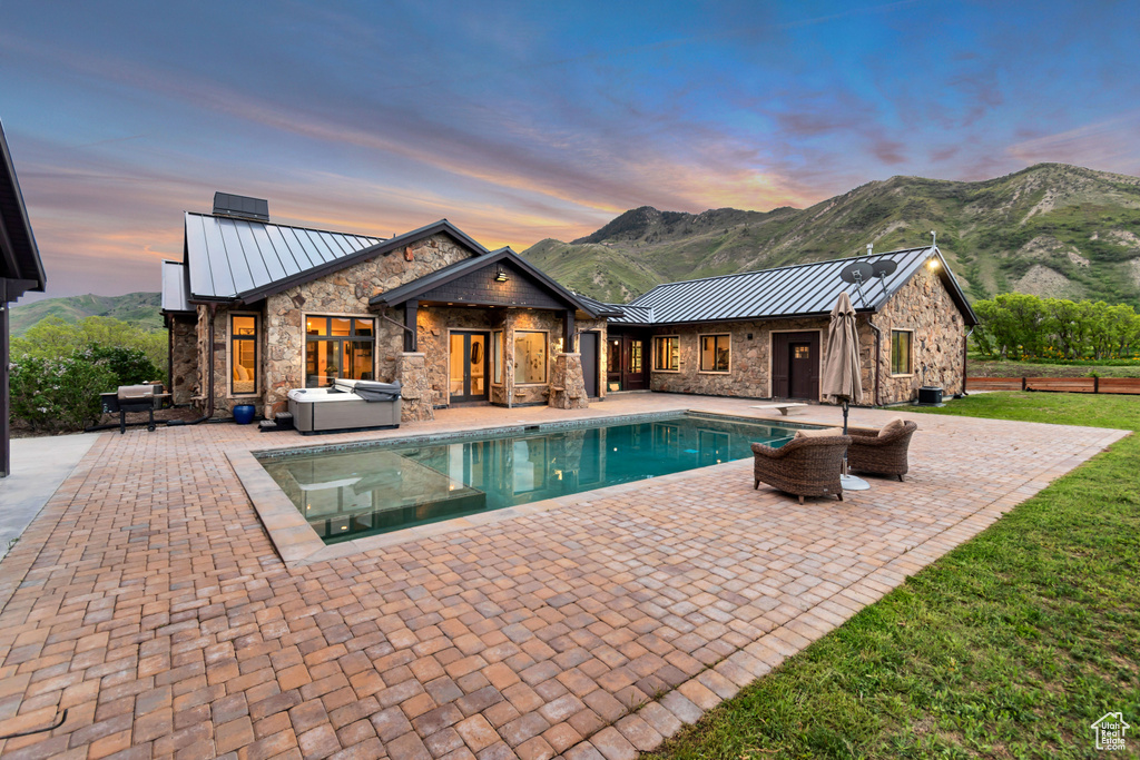 Pool at dusk featuring a hot tub, a patio, an outdoor pool, and a mountain view