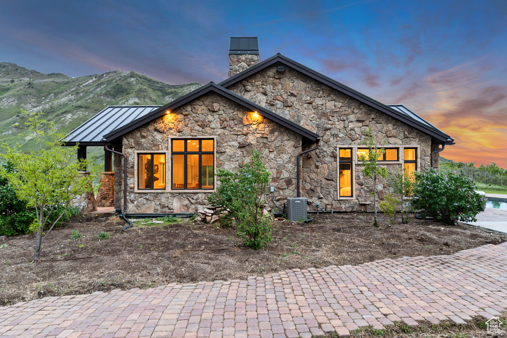 View of front facade featuring stone siding, a chimney, a standing seam roof, and central air condition unit