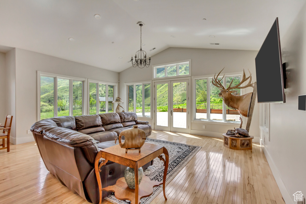 Living room with lofted ceiling, light wood-type flooring, french doors, a chandelier, and baseboards