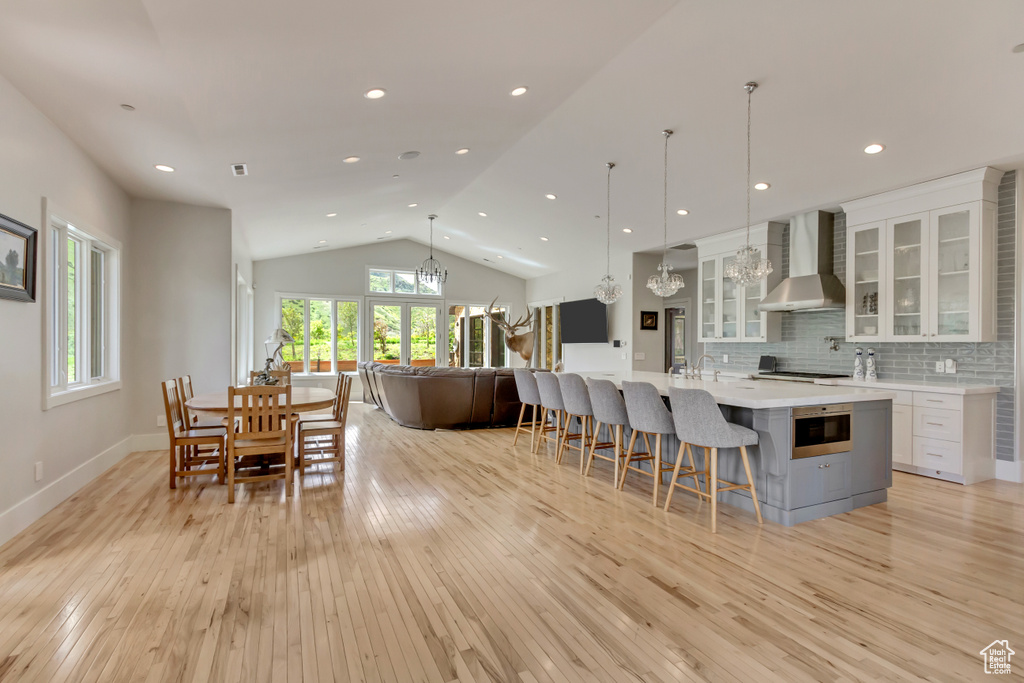 Kitchen featuring wall chimney exhaust hood, a chandelier, light wood-type flooring, light countertops, and lofted ceiling
