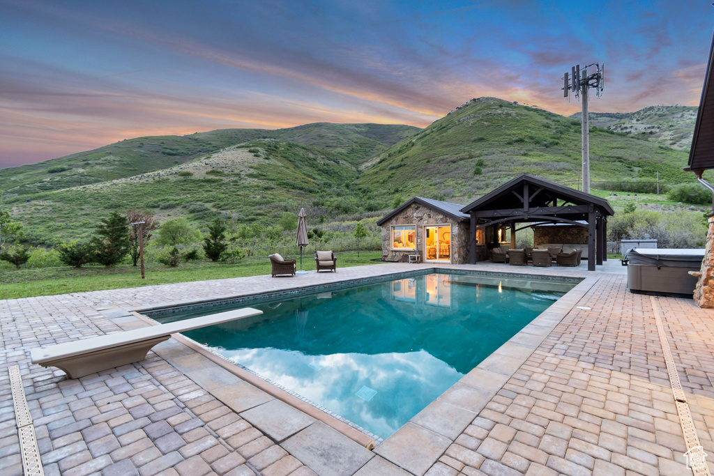 Pool at dusk with a hot tub, an outdoor hangout area, a patio area, an outdoor pool, and a mountain view