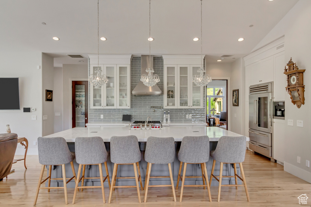 Kitchen with a chandelier, wall chimney exhaust hood, stainless steel built in fridge, decorative backsplash, and recessed lighting