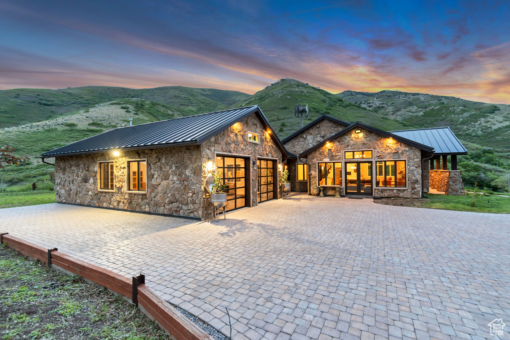 View of front facade featuring a standing seam roof, stone siding, an attached garage, metal roof, and a mountain view