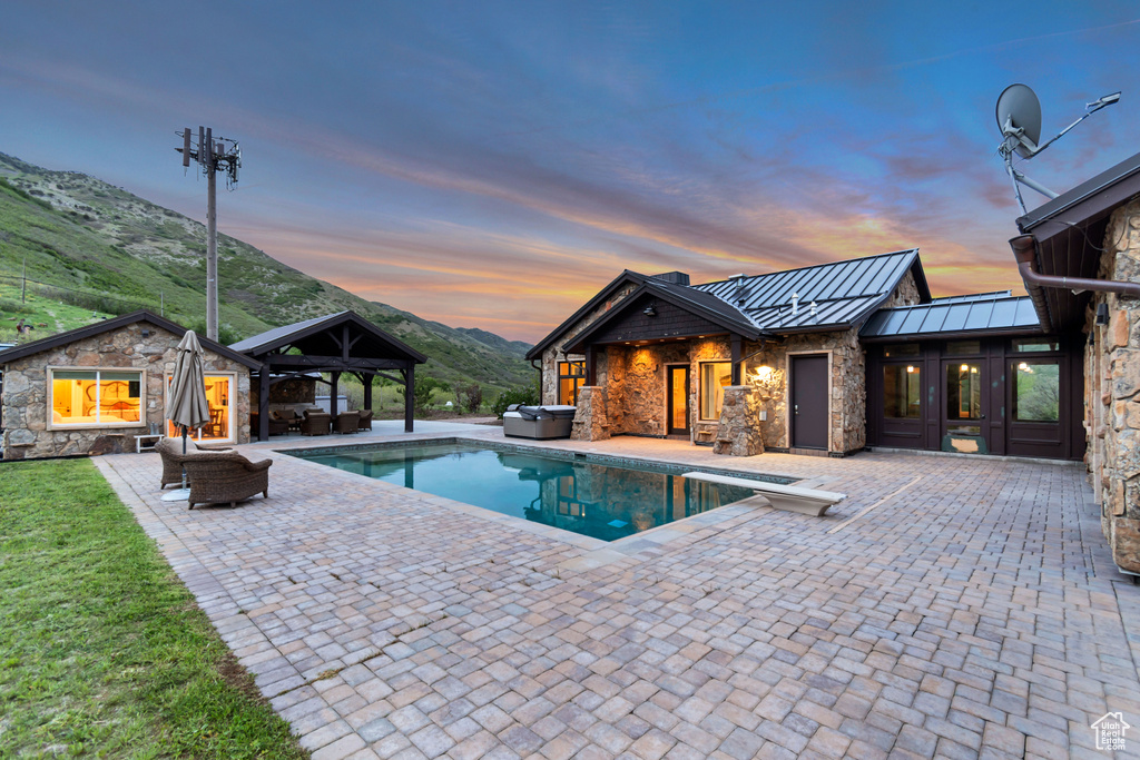 Pool at dusk with a gazebo, an outdoor pool, a patio, a covered hot tub, and a mountain view