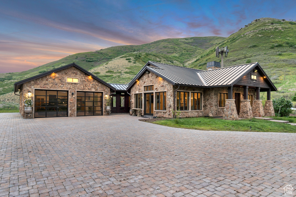View of front of property featuring a standing seam roof, stone siding, an attached garage, metal roof, and a mountain view