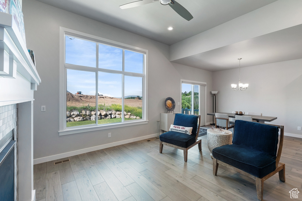 Living area with a fireplace, ceiling fan, baseboards, a chandelier, and light wood-style flooring