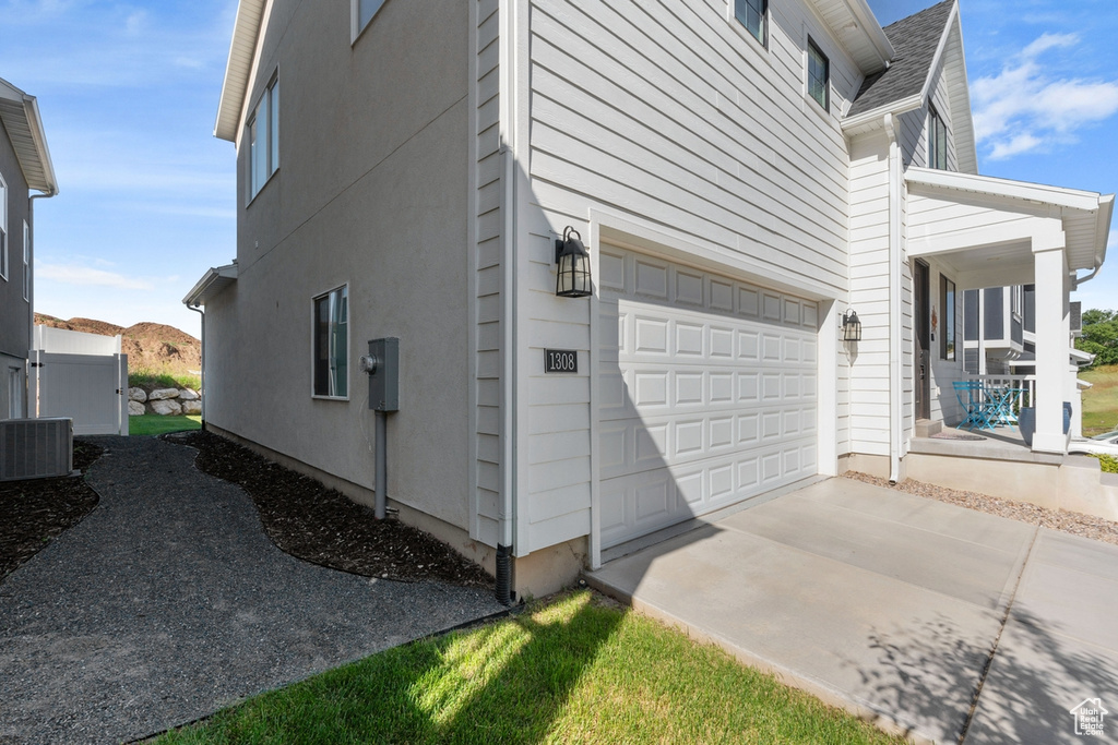View of side of property featuring an attached garage, central AC unit, a porch, and a shingled roof