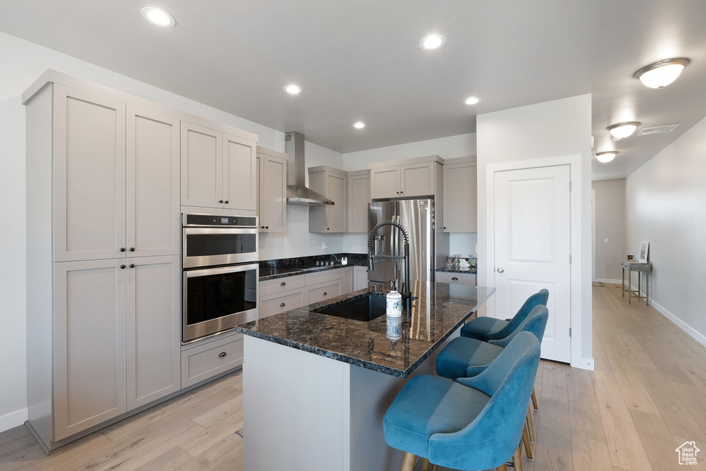 Kitchen featuring wall chimney exhaust hood, appliances with stainless steel finishes, light wood-type flooring, a breakfast bar, and recessed lighting