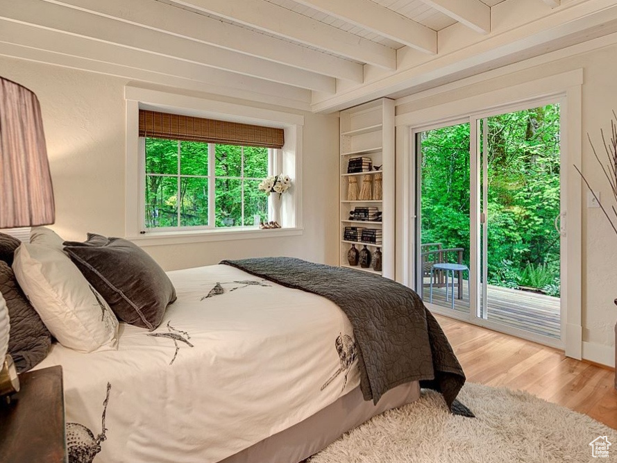 Bedroom featuring access to outside, beam ceiling, wood finished floors, and multiple windows