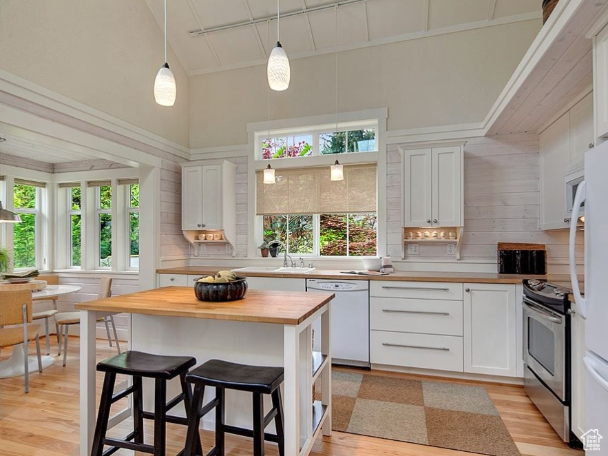 Kitchen with white appliances, wooden counters, high vaulted ceiling, light wood-style flooring, and white cabinets