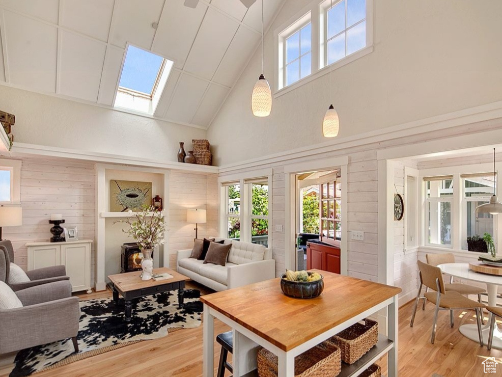 Living room featuring high vaulted ceiling, a skylight, light wood-style floors, wood walls, and plenty of natural light