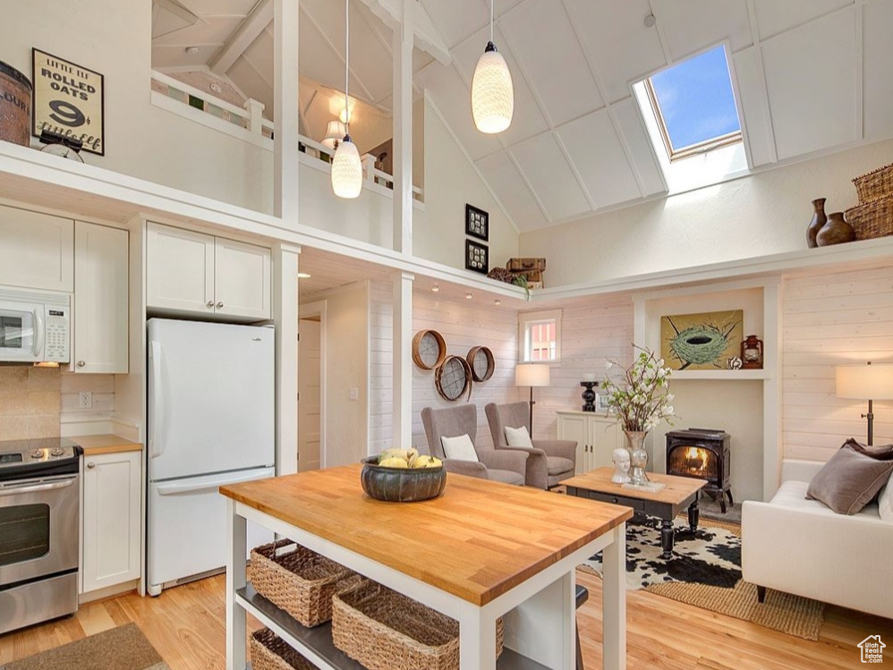 Kitchen with white appliances, a skylight, open floor plan, light wood finished floors, and high vaulted ceiling