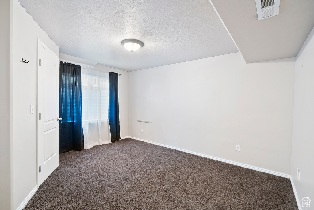 Unfurnished room featuring dark colored carpet and a textured ceiling