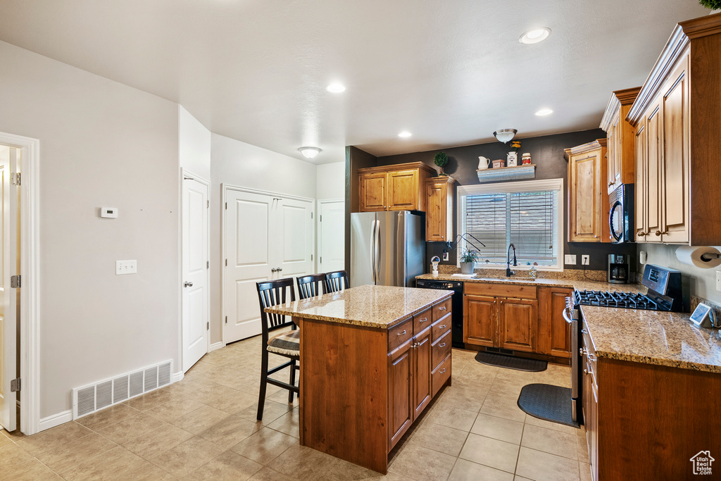 Kitchen featuring black appliances, a breakfast bar, a kitchen island, light stone countertops, and recessed lighting