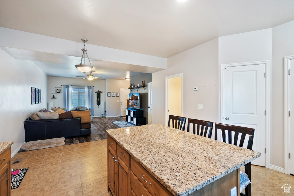 Kitchen featuring brown cabinets, ceiling fan, hanging light fixtures, light stone countertops, and a kitchen breakfast bar