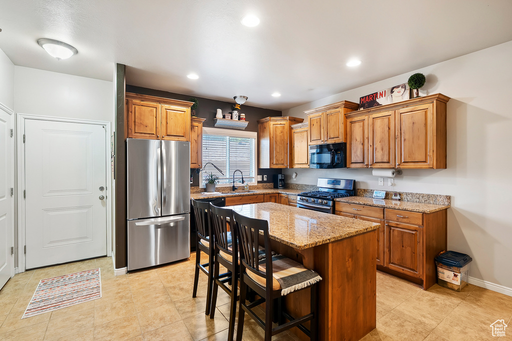 Kitchen featuring appliances with stainless steel finishes, brown cabinets, light stone counters, a center island, and recessed lighting