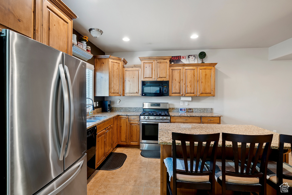 Kitchen featuring black appliances, light stone counters, a breakfast bar, recessed lighting, and light tile patterned floors