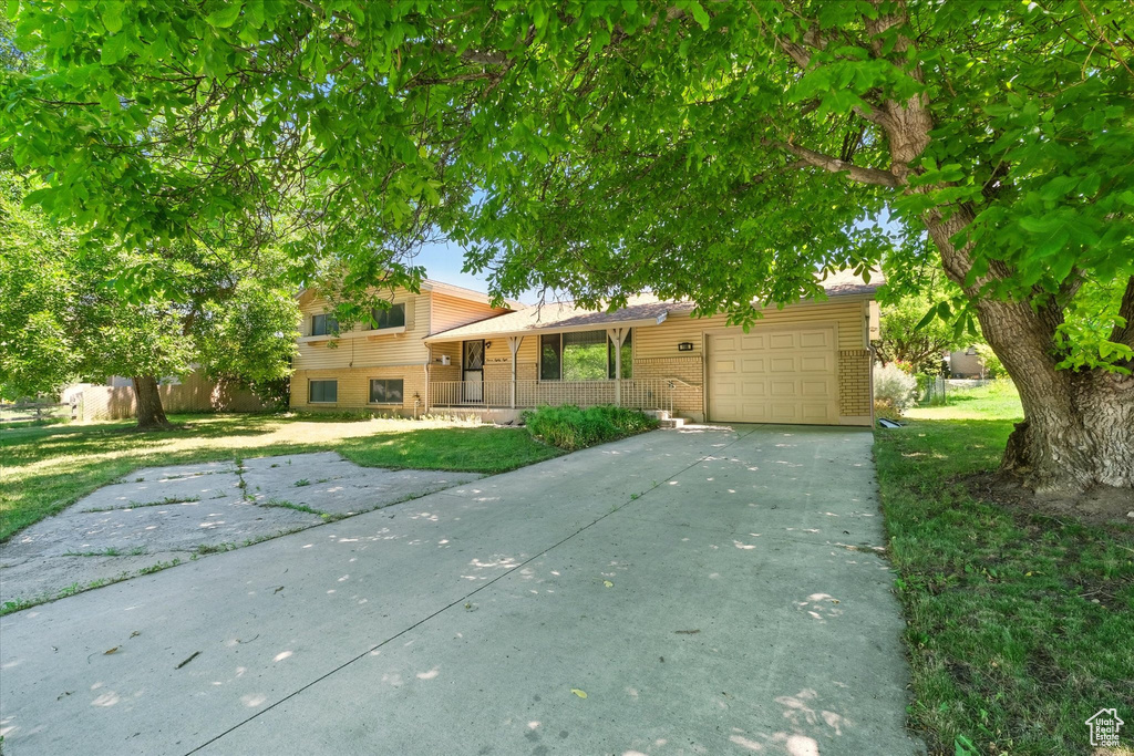 Tri-level home featuring brick siding, a garage, driveway, a porch, and a front lawn