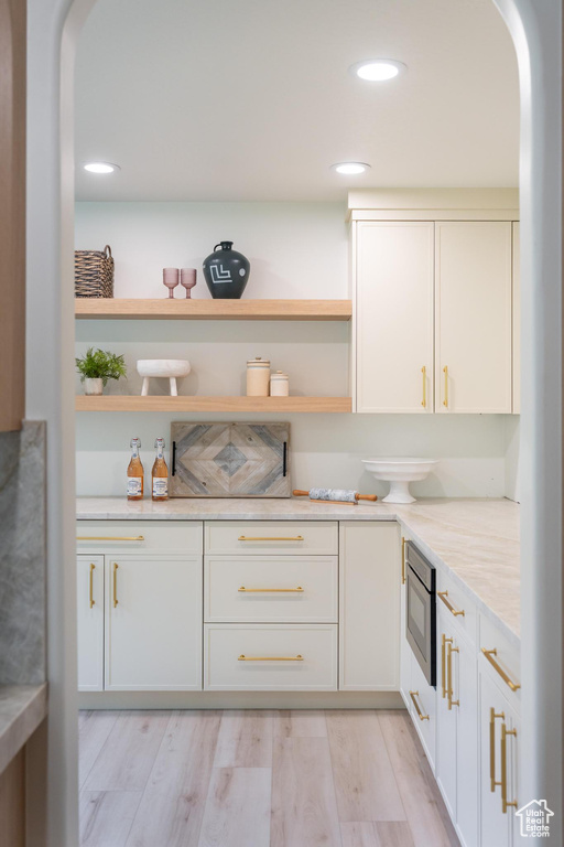 Kitchen featuring arched walkways, open shelves, light countertops, light wood-style floors, and recessed lighting