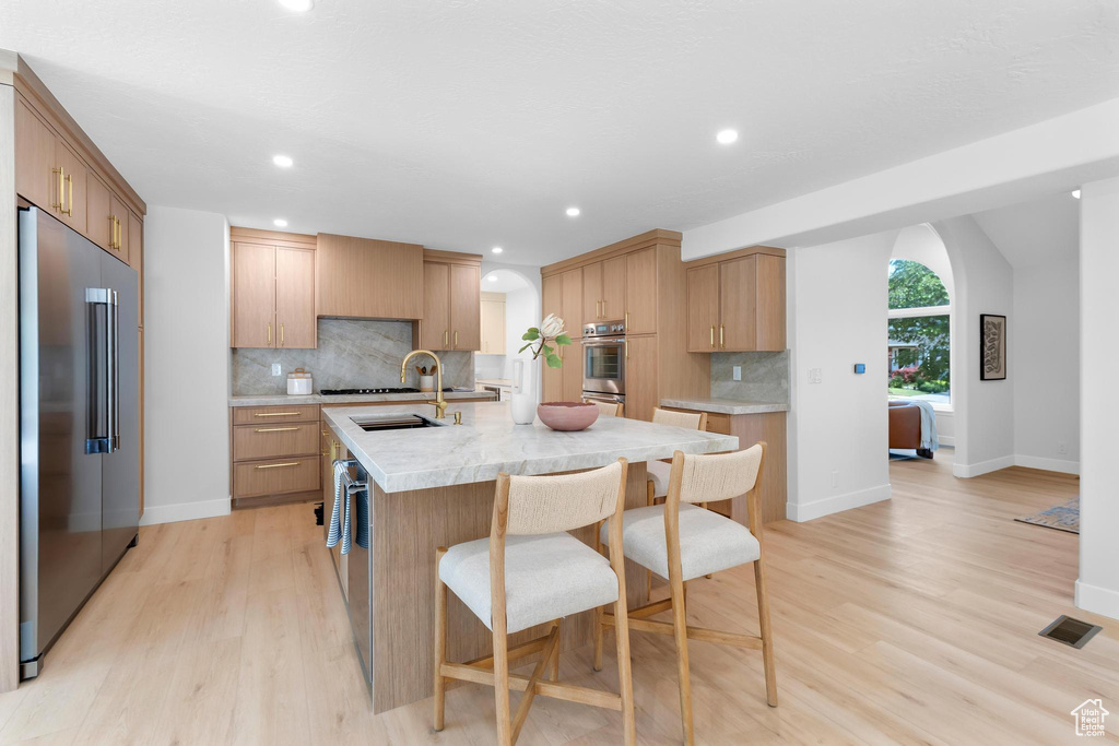 Kitchen with appliances with stainless steel finishes, light countertops, arched walkways, decorative backsplash, and light wood-type flooring