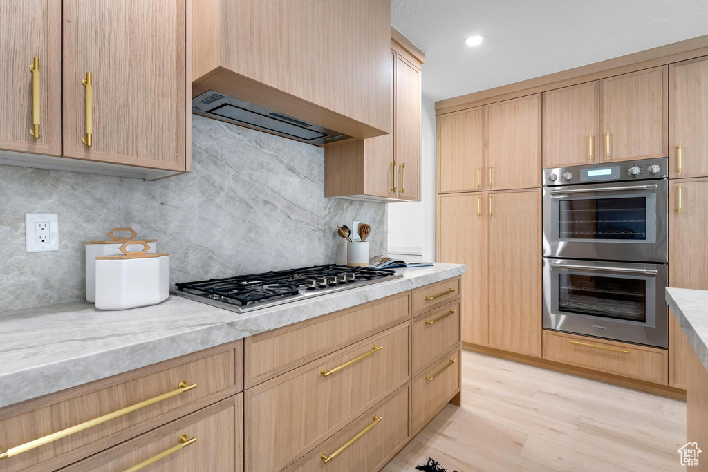 Kitchen featuring appliances with stainless steel finishes, light brown cabinets, decorative backsplash, and light wood-type flooring