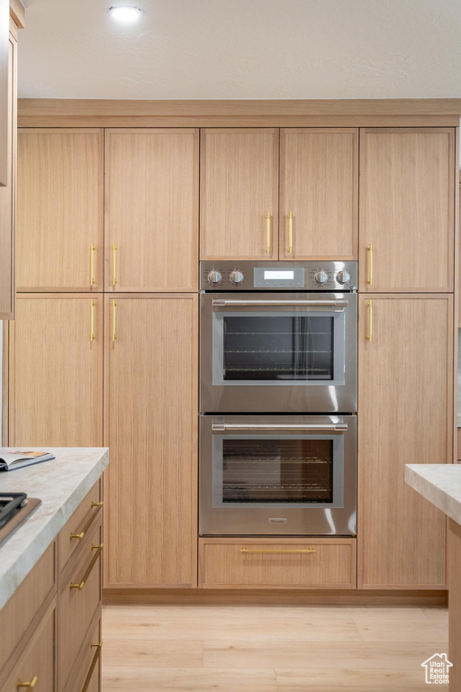 Kitchen featuring double oven, light brown cabinets, light wood-style floors, and light countertops