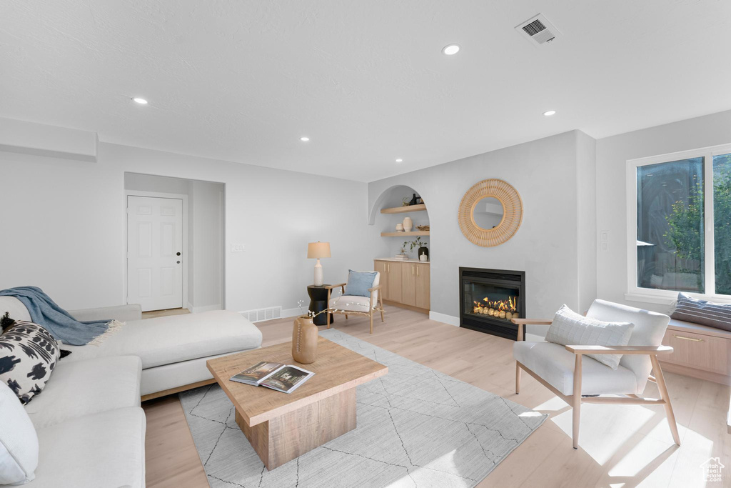 Living room featuring light wood-style flooring, a glass covered fireplace, recessed lighting, and baseboards